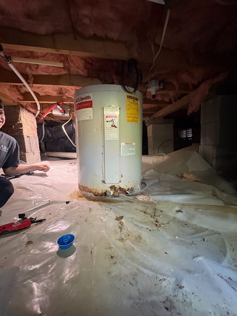 BEFORE — the old tank, corroded at the base and leaking onto the vapor barrier | Rusted, leaking water heater in a crawlspace in Angier, NC, before ARC Plumbing replaced it |