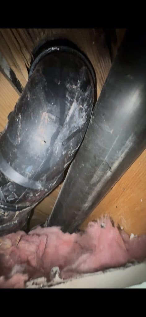 BEFORE — above the ceiling: the old ABS drain, set at an angle | Old black ABS toilet drain pipe above a ceiling with a leak in North Ridge, Raleigh, NC |