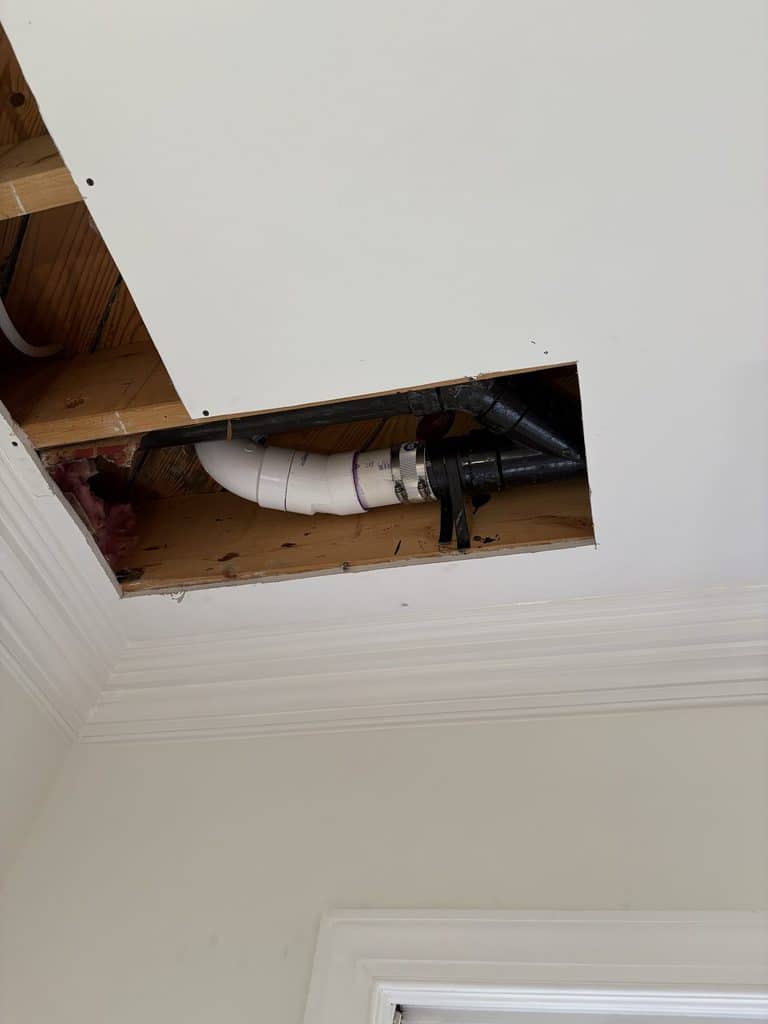 AFTER — the angled section cut out and replaced with new PVC | New white PVC toilet drain replacing old ABS pipe in a ceiling opening in Raleigh, NC