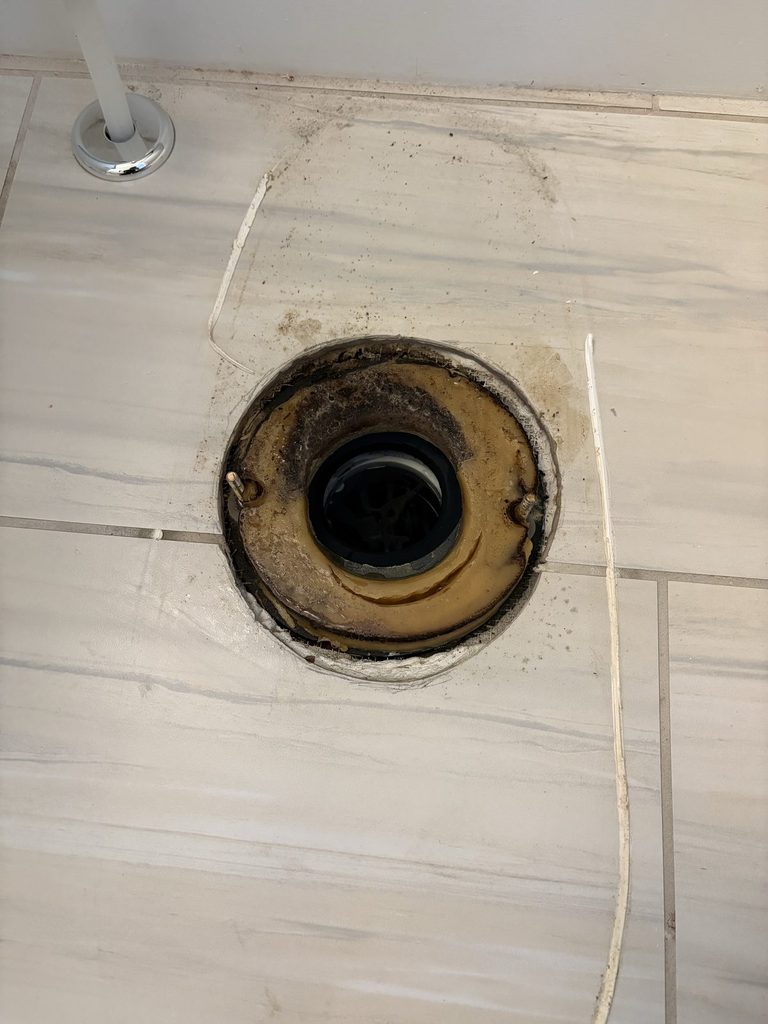 BEFORE — the cracked flange, with the toilet pulled | Cracked toilet flange in a bathroom floor in North Ridge, Raleigh, NC, before repair |
