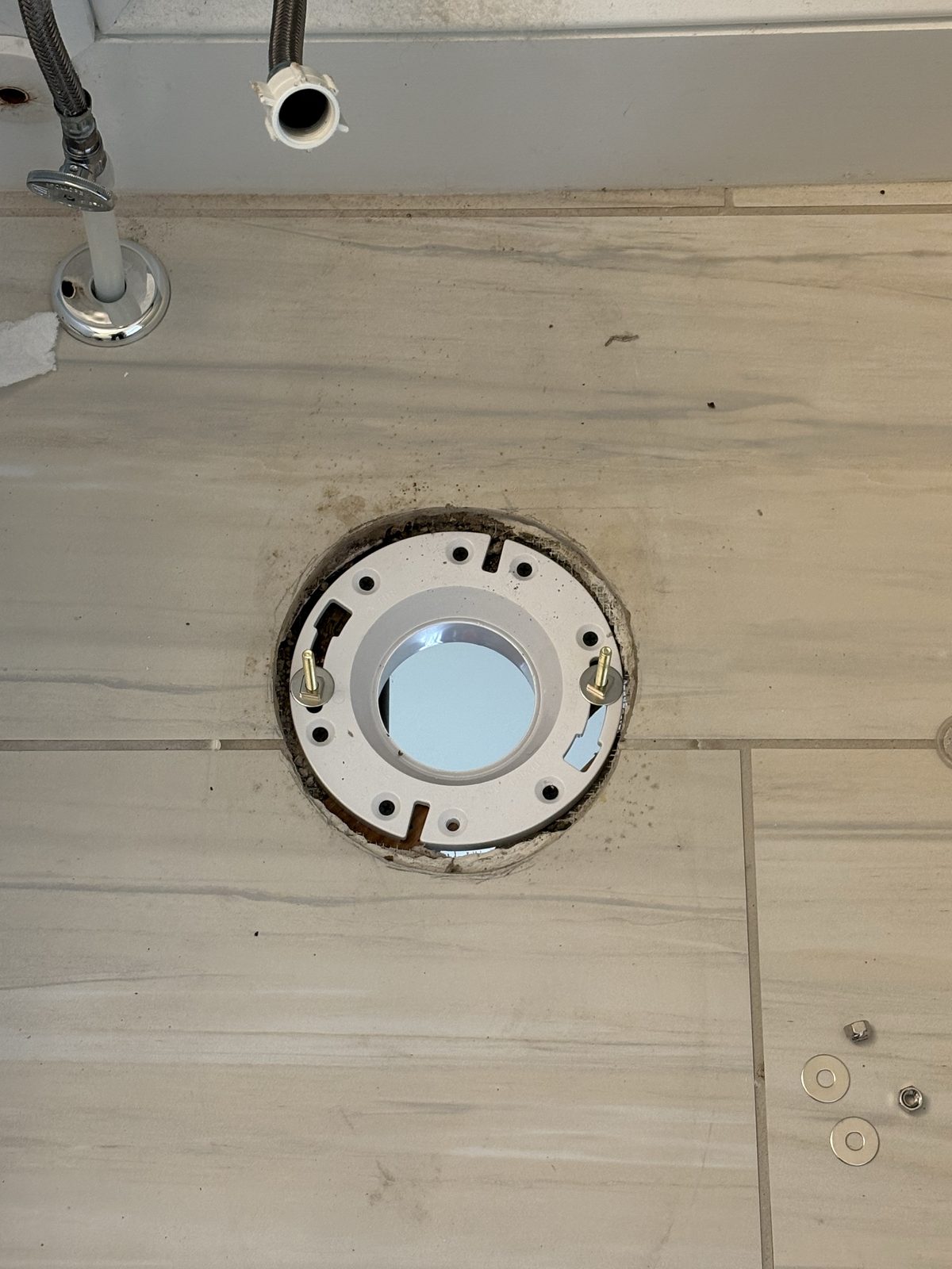 New PVC toilet flange installed on a bathroom floor, replacing a cracked flange on angled ABS pipe