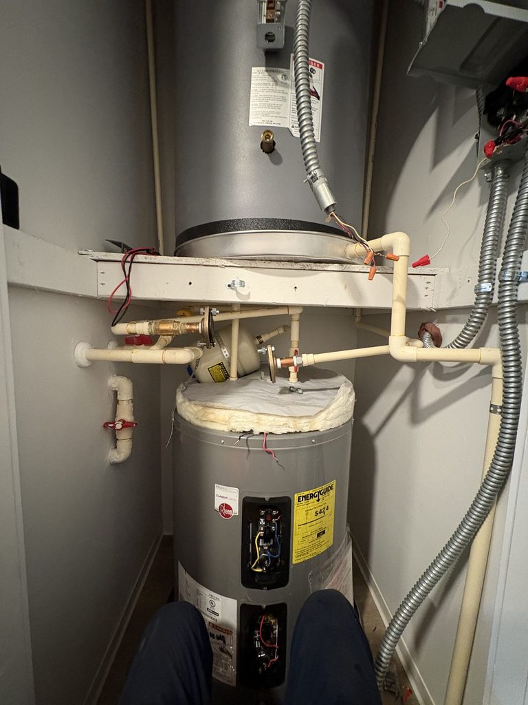 BEFORE — two stacked 40-gallon heaters and the recirculation pump that kept them running | Two stacked 40-gallon electric water heaters with a recirculation pump in a Raleigh apartment closet |