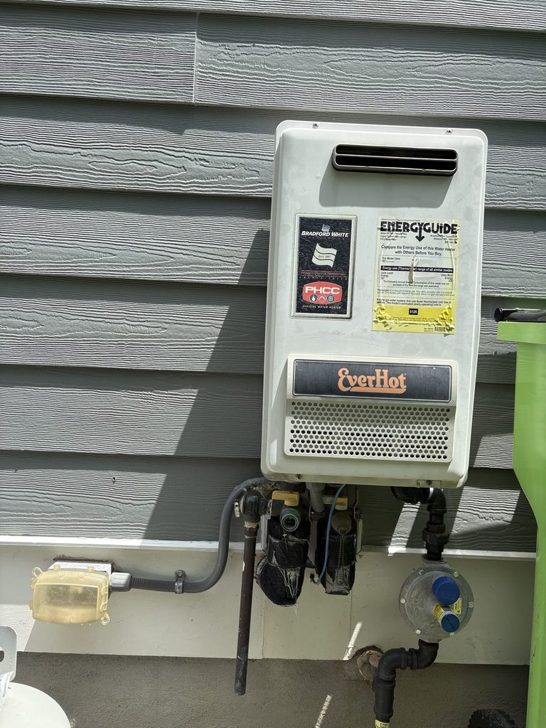 BEFORE — the 20-year-old Bradford White EverHot tankless | Old Bradford White EverHot tankless water heater on the exterior wall of a Fuquay-Varina, NC home |