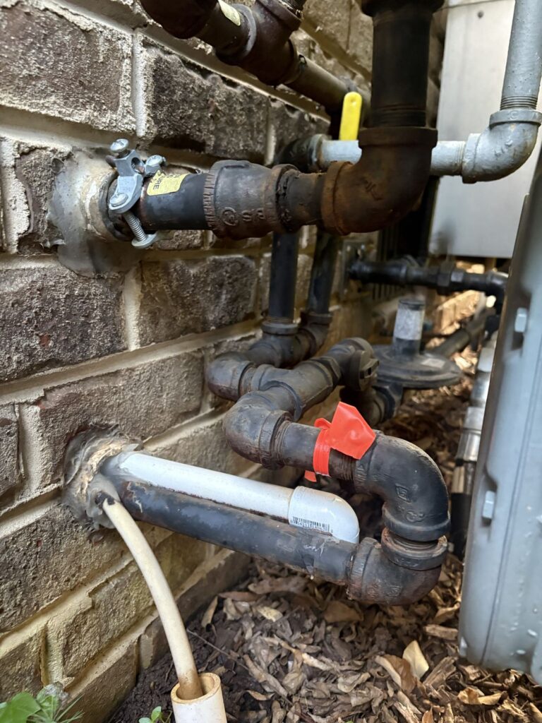 Corroded gas piping entering a brick home in Westbury, Raleigh, NC, with tape marking the leaking fitting